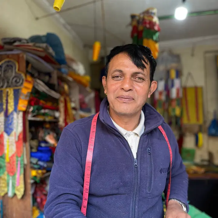 A tailor with a measuring tape round his neck at the counter of his cloth shop in Kathmandu